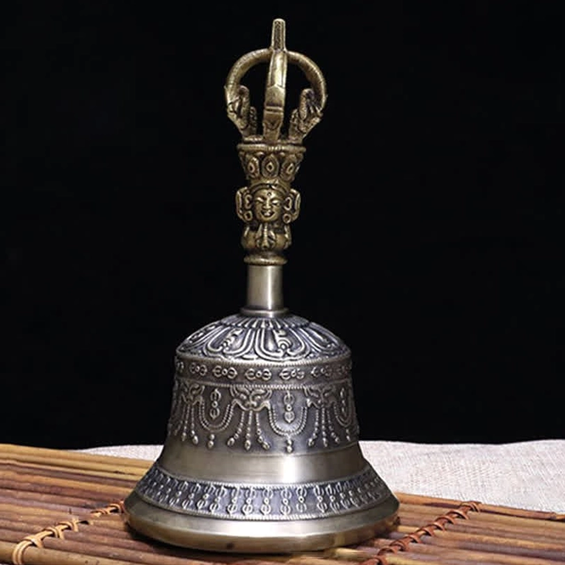 Single Tibetan ritual bell side view showing intricately carved handle and bell body in antiqued silver-grey tone