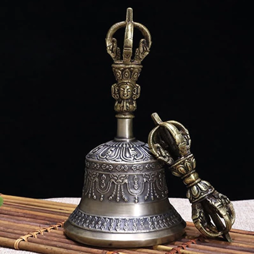 Close-up three-quarter view of handcrafted Tibetan meditation bell and five-pronged vajra dorje on bamboo mat, showing intricate carved details