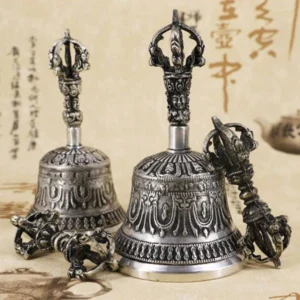 Tibetan meditation bell and vajra dorje copper set displayed on antique calligraphy background, showing intricate carved religious patterns in aged silver tone
