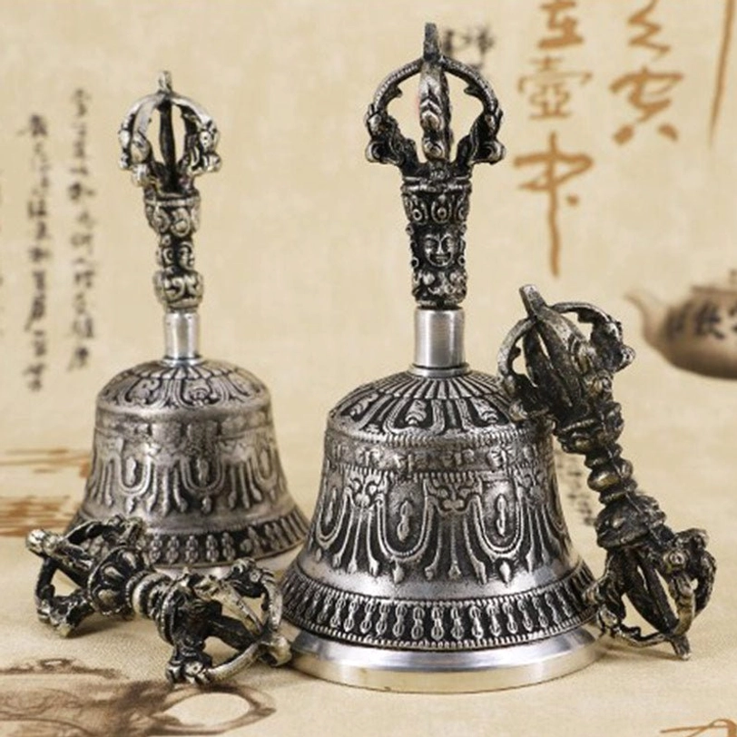 Tibetan meditation bell and vajra dorje copper set displayed on antique calligraphy background, showing intricate carved religious patterns in aged silver tone