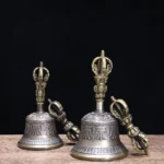 Tibetan meditation bell and vajra dorje set pair with aged bronze and silver-grey patina, displayed on wooden table with black backdrop