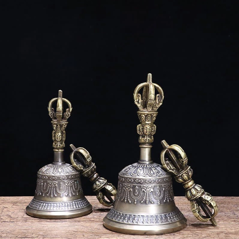 Tibetan meditation bell and vajra dorje set pair with aged bronze and silver-grey patina, displayed on wooden table with black backdrop