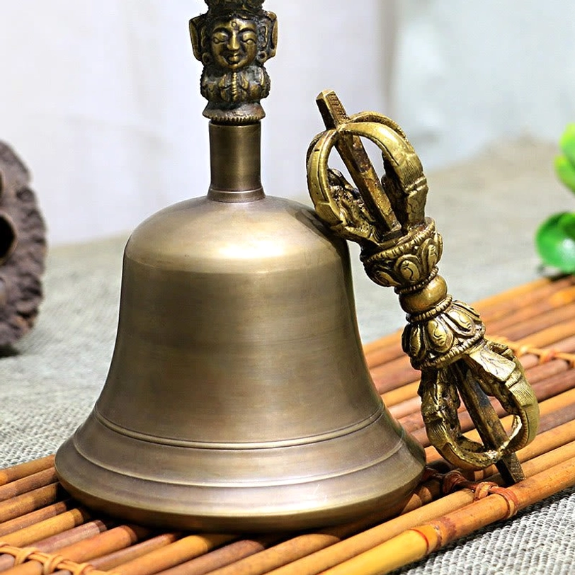 Low angle view of Tibetan bell and vajra dorje set on burlap and bamboo mat, showing brushed bronze tone and paired ritual instruments