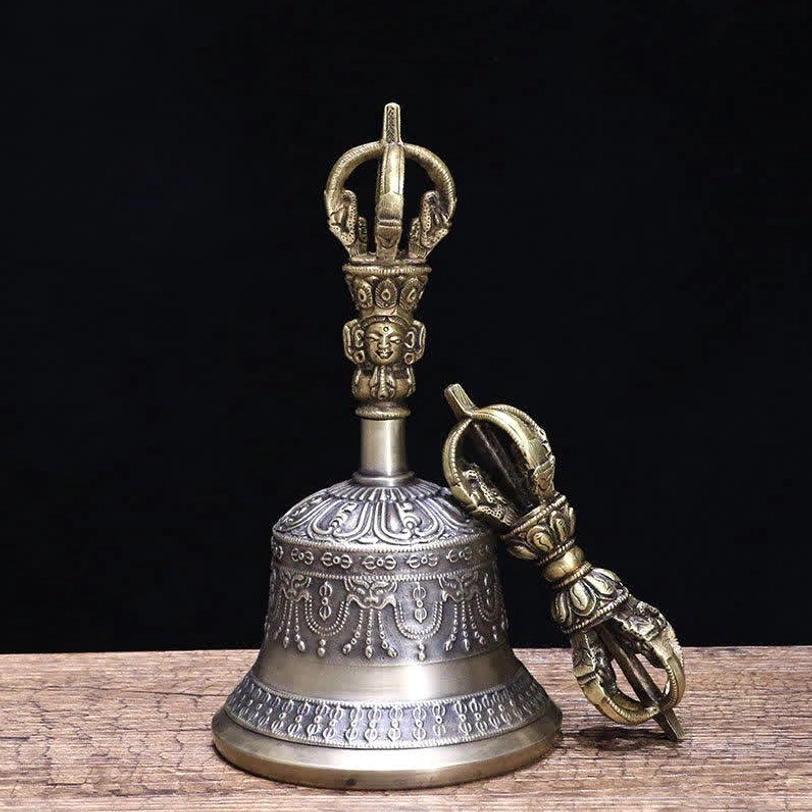 Tibetan meditation bell and matching vajra dorje three-quarter front view on light fabric backdrop with wooden table