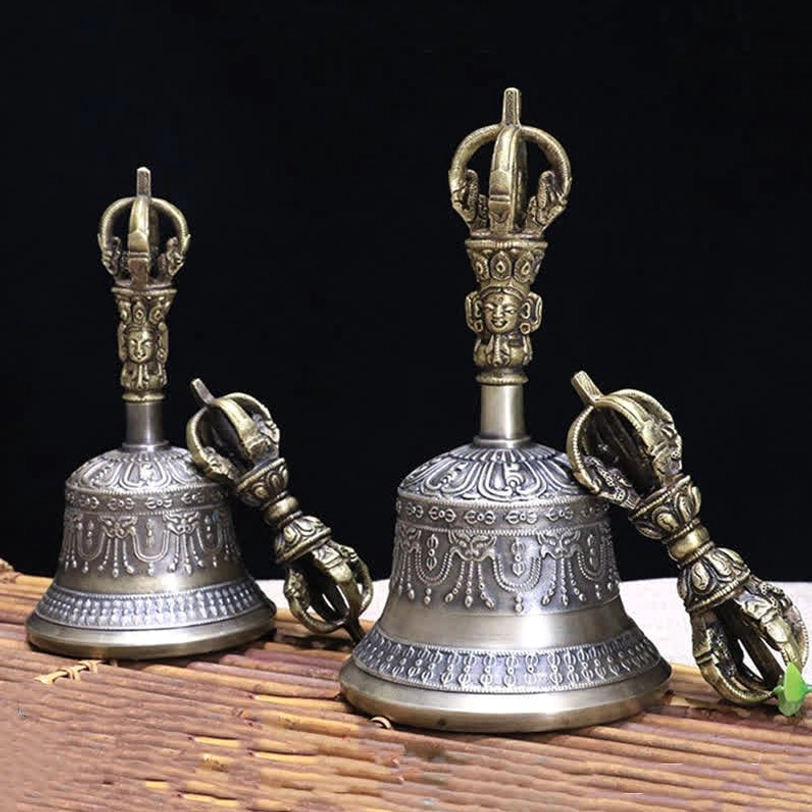 Two Tibetan meditation bells with matching embossed designs and five-pronged vajra dorje on bamboo mat display