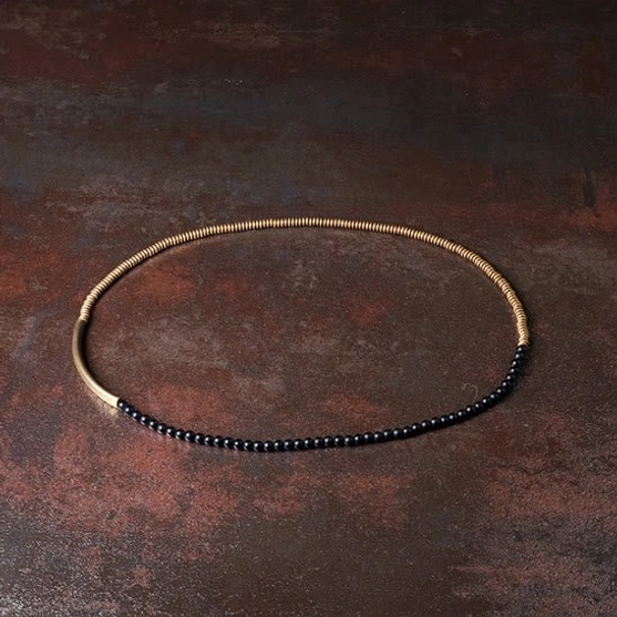 Single wrap minimalist Tibetan bracelet flat lay with small black beads, wrapped brass wire, and brass tube on rustic surface