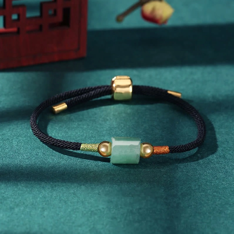 Black Tibetan woven lucky bracelet with light green barrel bead and gold metal accents on retro Chinese desktop