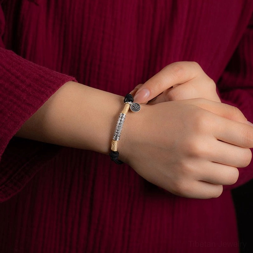 Black braided Tibetan blessing bracelet worn on wrist with maroon clothing background