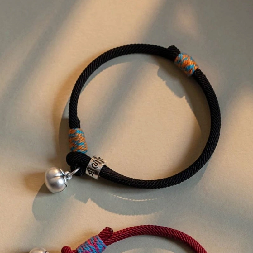 Single black braided om mani padme hum bracelet with colorful woven trim and silver charm close-up