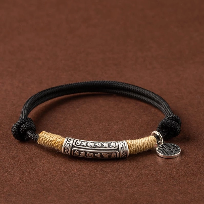 Black cord Tibetan braided bracelet with sterling silver om mani padme hum tube on dark background