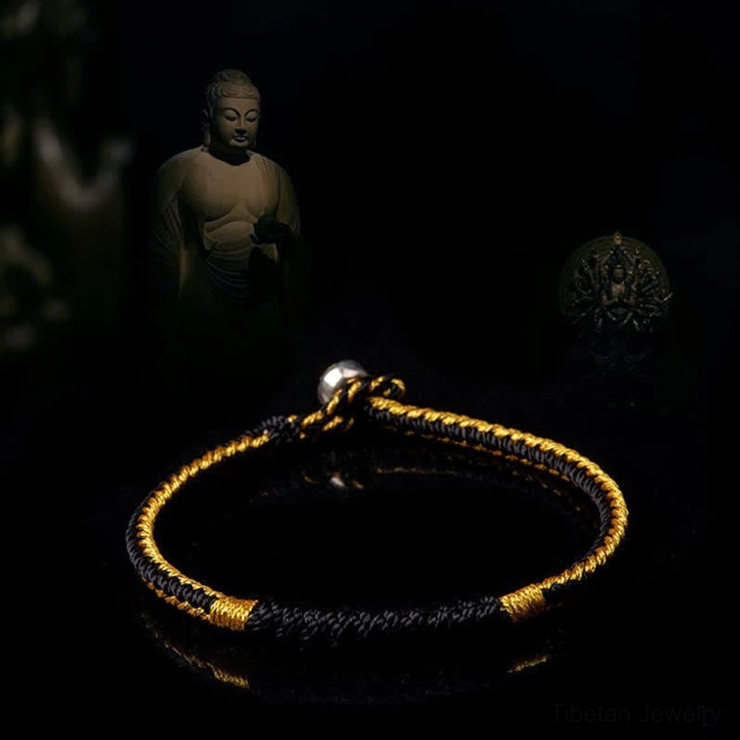 Black and gold Tibetan braided lucky bracelet with twisted weave pattern and silver buckle on dark Buddhist background