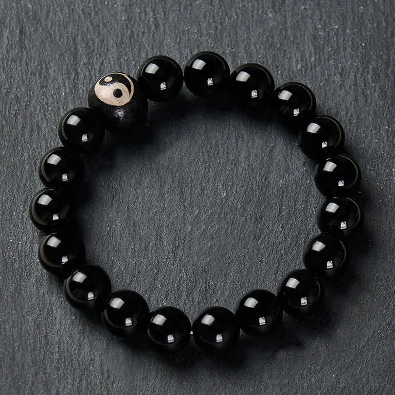 Black Obsidian Yin Yang bracelet flat lay on grey matte background, Yin Yang bead positioned on left side of elastic cord