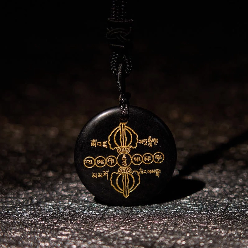 Front view of Vajra Dorje black obsidian crystal pendant with intricate golden Sanskrit and Dorje patterns, flat lay on glittery background