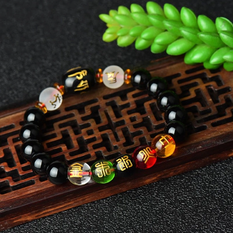 Complete handmade Tibetan black onyx bracelet with mixed colored Buddhist beads and hand-engraved mantra barrel displayed on carved wooden base