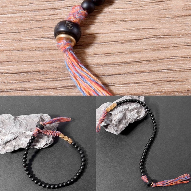 Close-up detail of Tibetan black onyx tassel bracelet showing braided tassel, black decorative bead, and artisan craftsmanship on wood