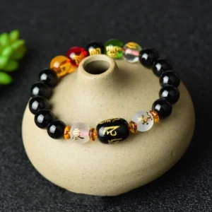 Tibetan black onyx luck bracelet with engraved mantra beads displayed on ceramic pot with green botanical accents, top-down side view