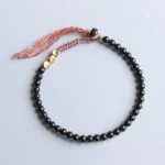 Handmade Tibetan black onyx tassel bracelet with round polished beads, gold metal spacers, and colorful woven tassel on light background