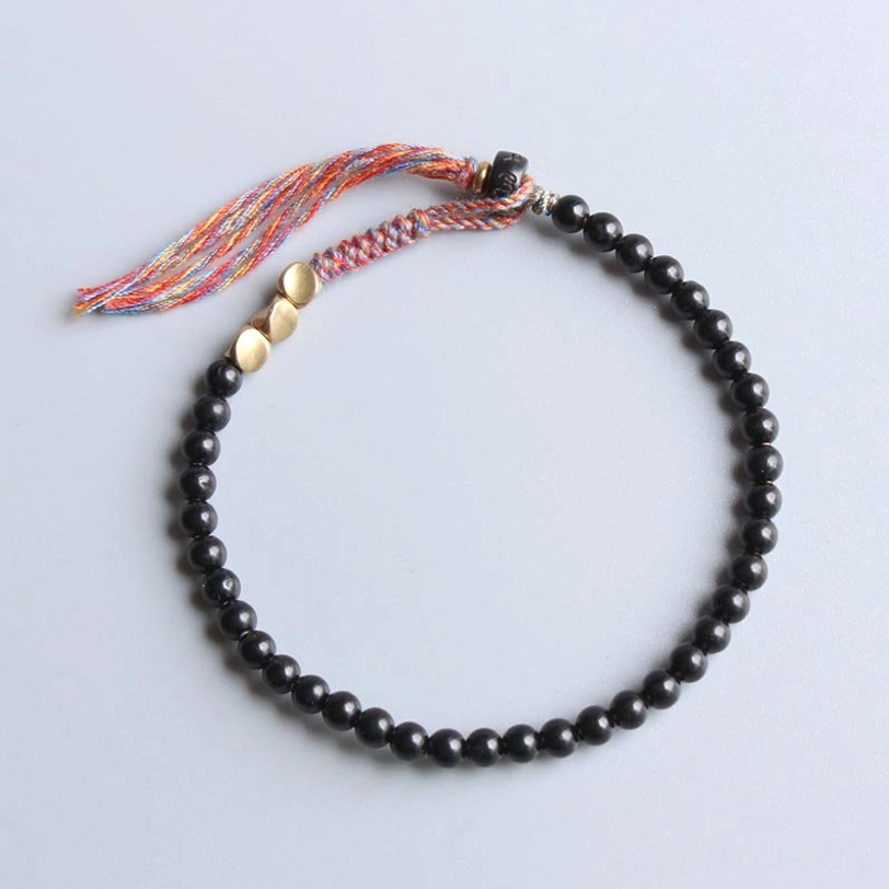 Handmade Tibetan black onyx tassel bracelet with round polished beads, gold metal spacers, and colorful woven tassel on light background