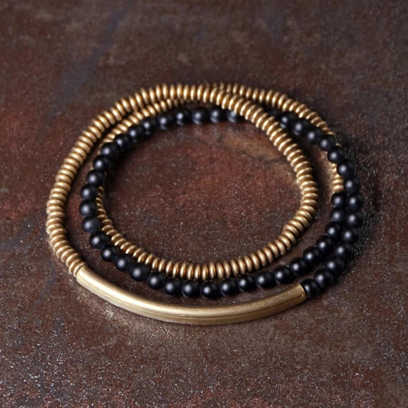 Black onyx triple wrap protection bracelet with bronze brass accents on dark surface showing matte stone texture