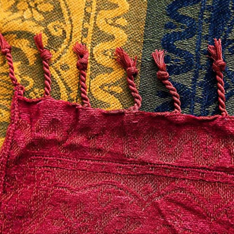 Top-down view of Tibetan blanket border featuring thick twisted rope tassels and burgundy fabric with multi-color block design