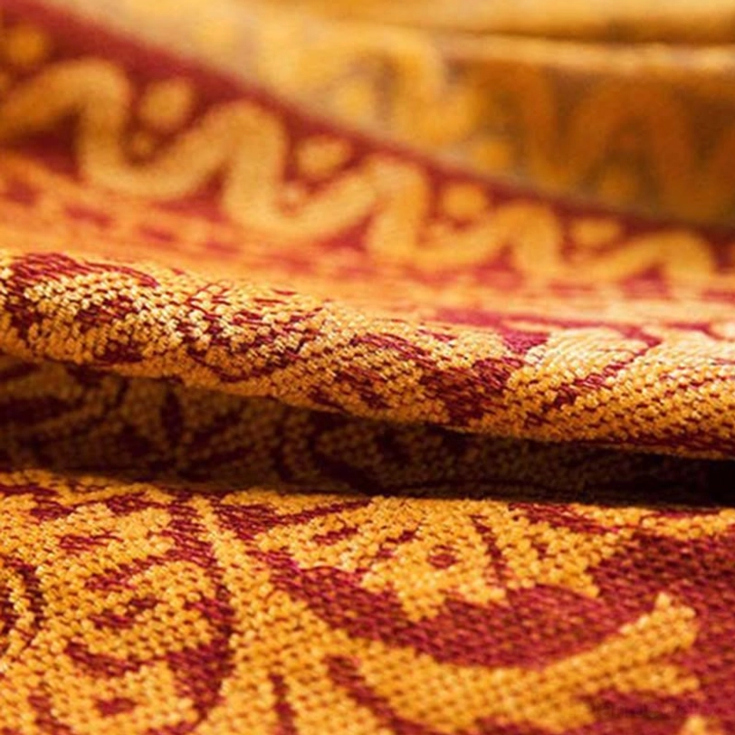Extreme close-up of Tibetan handwoven blanket fabric showing intricate scroll damask pattern in yellow and burgundy tones