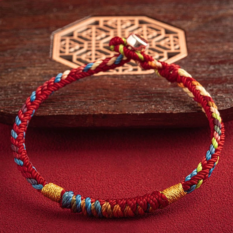 Finished handcrafted Tibetan multicolor protection bracelet with blessing knot displayed on wooden coaster, red background