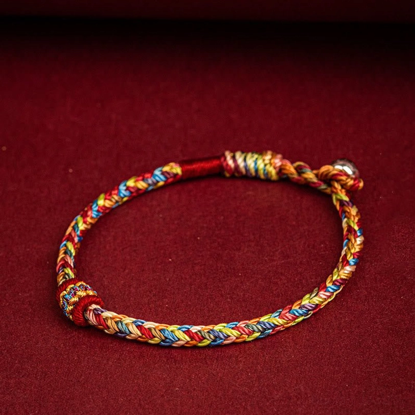 Colorful Tibetan prayer string bracelet flat lay with red accent knots and metal clasp on dark fabric background