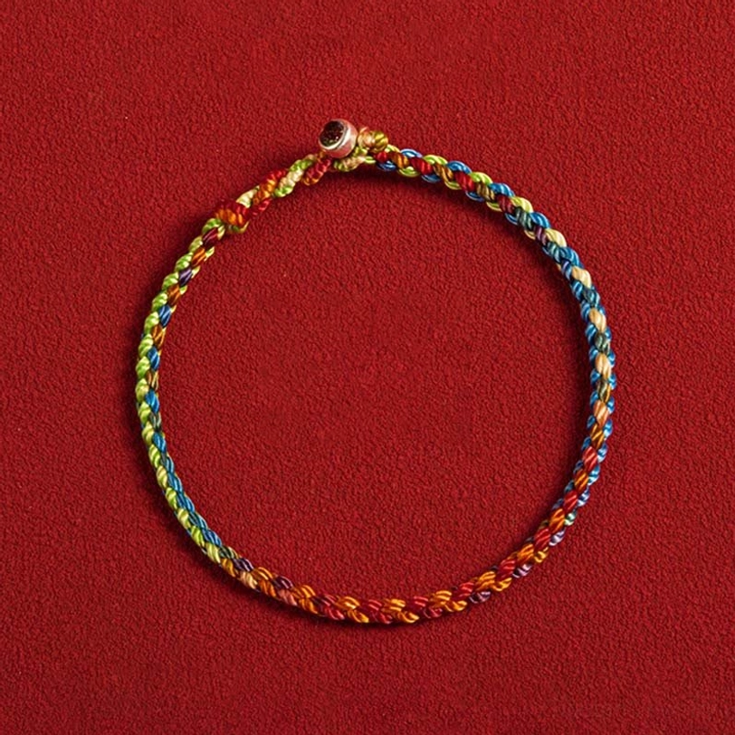 Flat lay of colorful woven Tibetan bracelet showing gradient thread details and metal toggle clasp