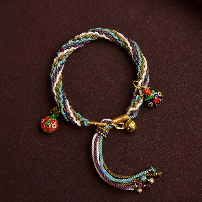Flat lay overhead view of Tibetan swallowing beast bracelet with multicolor woven cord, three golden enamel charms and decorative tassel