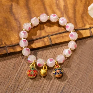 Single Tibetan blessing bracelet with fluorescent pink liuli glass beads and gold swallowing beast charm close-up