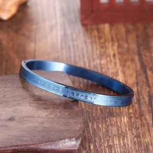Tibetan titanium steel blessing bracelet with sacred engravings, blue finish, overhead view on wooden coaster
