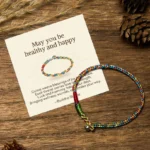 Tibetan multicolored blessing bracelet with 925 silver clasp displayed next to personalized greeting card on wooden desk