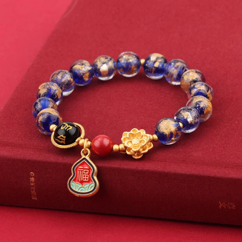 Tibetan blue spotted Liuli glass bracelet with gold accents displayed on red book surface