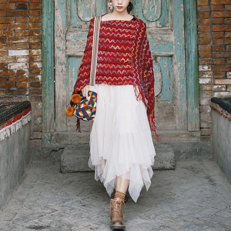 Boat neck tibetan ethnic knit poncho with tassel hem and ankle boots walking in front of retro brick wooden door yard