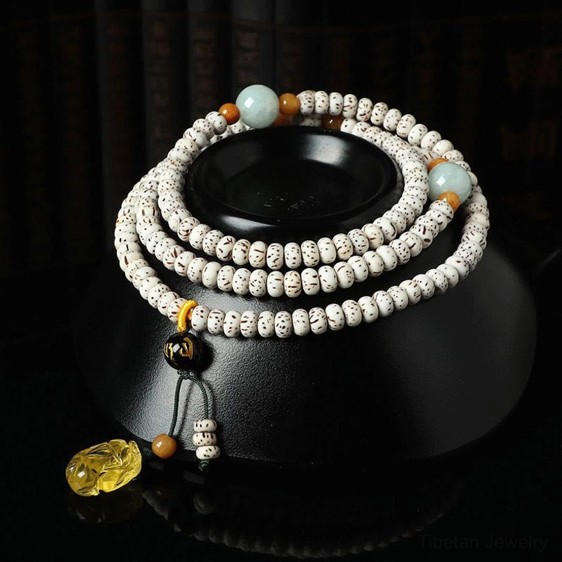 Tibetan bodhi seed mala bracelet with amber accent and pixiu pendant, displayed on black ceramic meditation base