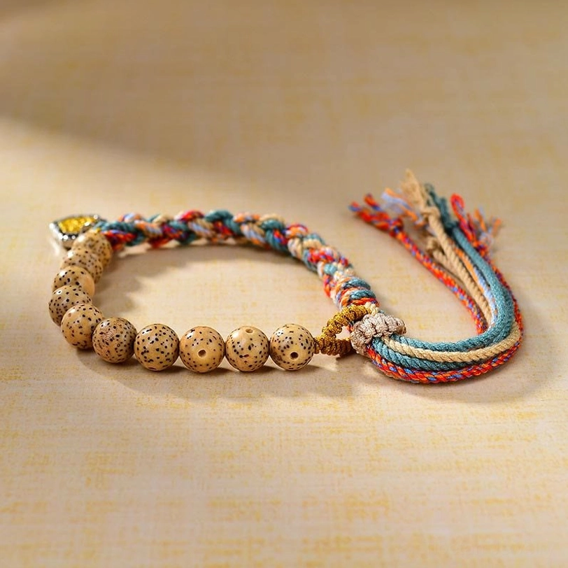 Side view of handwoven Tibetan protection bracelet showing detailed bodhi seed beads, colored rope weave, and metal goddess amulet