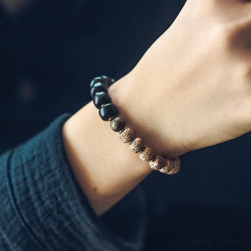 Worn two-tone Tibetan Bodhi bracelet with cube black beads and brass hardware on wrist close-up with dark green clothing