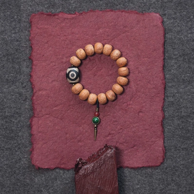 Full Tibetan bodhi seed dzi bead bracelet with hanging pendant on wine-red fabric overhead flat lay
