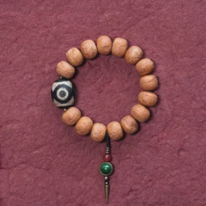 Tibetan bodhi seed dzi bead mala bracelet overhead view with three-eyed dzi focal bead and brass charm on wine-red background