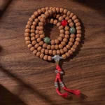 108 bodhi seed mala with three-eye dzi bead displayed on wooden surface, showing complete necklace arrangement with red agate spacers and silver accents