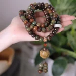 Tibetan 108 bodhi seed mala bracelet with Dzi bead and carved wooden tassel, earth-tone Dunhuang colors held in hand