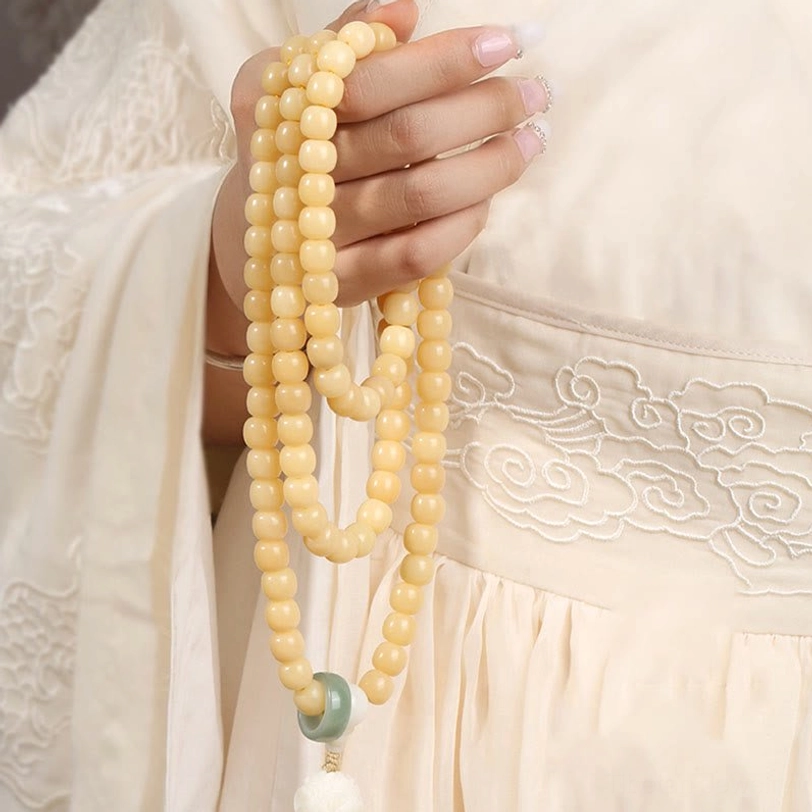Hands holding multi-turn bodhi seed prayer mala bracelet with beige beads and green spacer