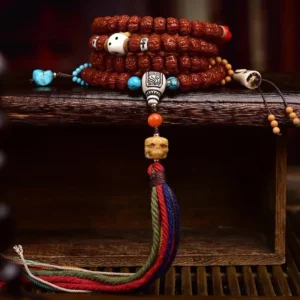 Stacked 108 Bodhi seed prayer mala with turquoise spacers, bone skull beads, carved guru bead, and woven tassel on wooden shelf