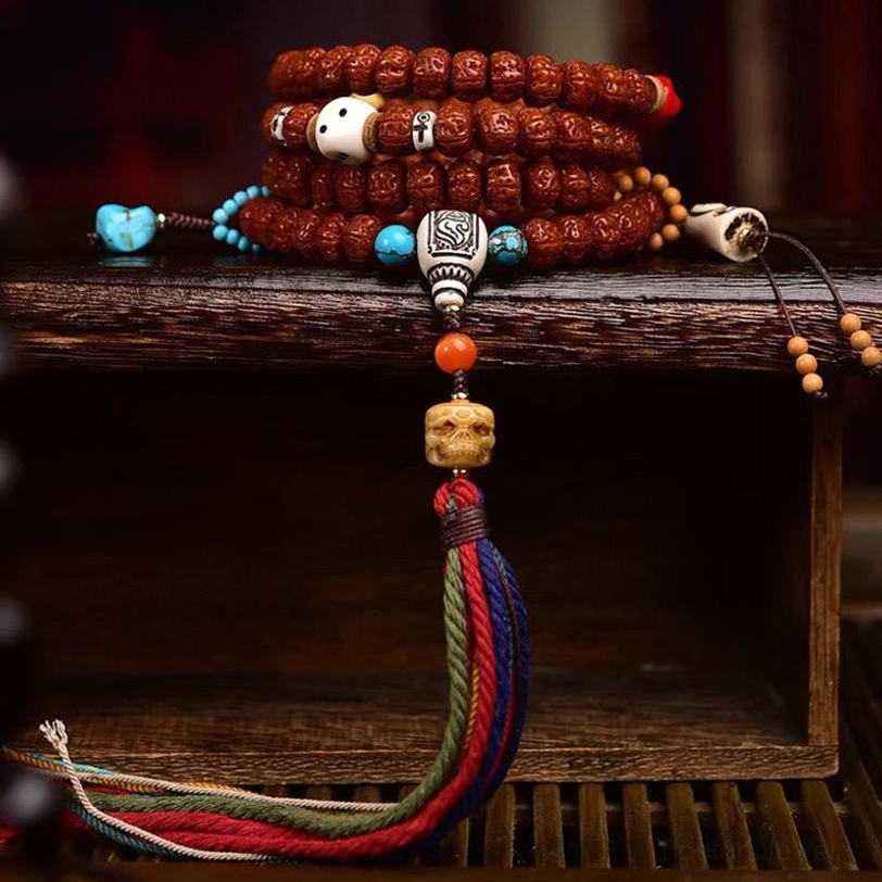 Stacked 108 Bodhi seed prayer mala with turquoise spacers, bone skull beads, carved guru bead, and woven tassel on wooden shelf