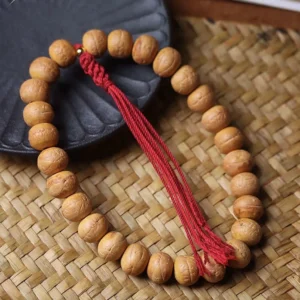 Tibetan prayer mala beads flat lay on woven cushion displaying long red tassel and plump bodhi seeds