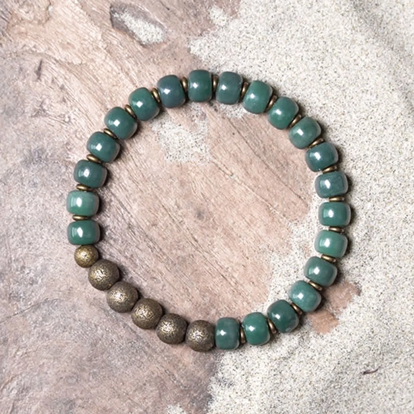 Tibetan cyan bodhi seed copper bracelet detail shot on sandy wooden surface, showing barrel-shaped matte green beads with bronze metal accents