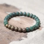 Tibetan bodhi seed copper bracelet flat lay on wooden surface, showing matte dark green barrel beads alternating with textured bronze spacer beads