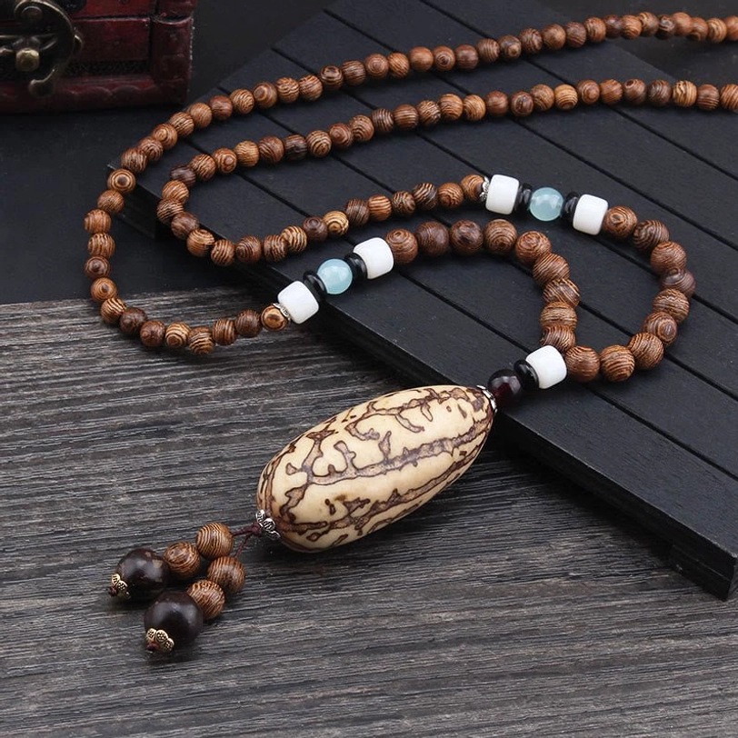 Tibetan bodhi seed necklace with large thousand-eyed pattern pendant and ethnic spacer beads on dark wood surface