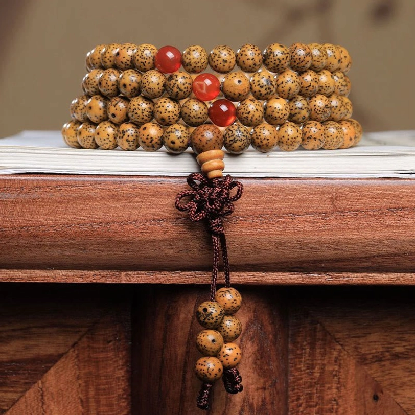 Tibetan 108 bodhi seed and red agate mala bracelet with braided tassel, displayed on wooden desk with book - top-down view
