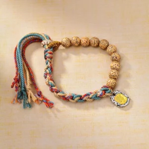 Tibetan multicolor bodhi seed bracelet with Zakiram goddess wealth charm and adjustable tassel, overhead flat lay view on neutral background
